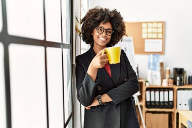 Genç Afro-Amerikan kadın gülerek ofiste kahve içiyor.