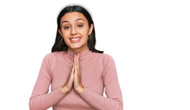 Gündelik kıyafetler giyen genç İspanyol kız ellerinin birarada dua ederek af diliyor kendinden emin bir şekilde gülümsüyor.. 