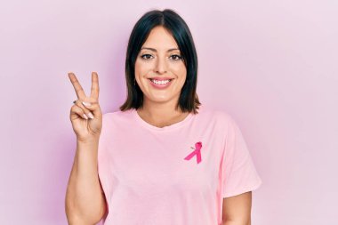 Gömleğine pembe kanser kurdelesi takmış genç İspanyol kadın kameraya bakıp zafer işareti yapıyor. İki numara.. 