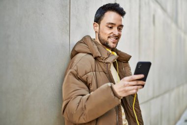 Genç İspanyol adam şehirde akıllı telefon ve kulaklık kullanarak mutlu gülümsüyor..