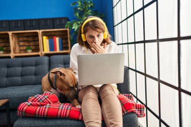 Genç ve güzel bir kadın, dizüstü bilgisayarla koltukta oturup ağzını eliyle kapatıyor, şok geçiriyor ve hata yapmaktan korkuyor. şaşırmış ifade 