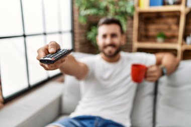 Genç İspanyol adam evde kahve içiyor ve televizyon seyrediyor.