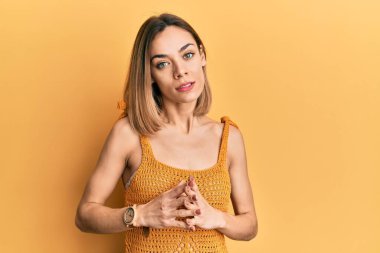 Sarışın, sıradan sarı tişörtler giyen genç bir kadın ellerini birleştirip gülümseyerek gevşemiş ve neşeli bir şekilde gülümsedi. Başarı ve iyimserlik 