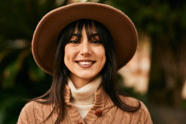 Parkta gülümseyen, kışlık şapkalı esmer kadın.