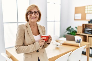 Orta yaşlı sarışın kadın kahve içiyor. Mimarlık stüdyosunda çalışıyor.
