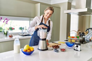 Genç sarışın kadın gülümsüyor. Kendine güveni tam. Smoothie 'yi sıvılaştırıyor.
