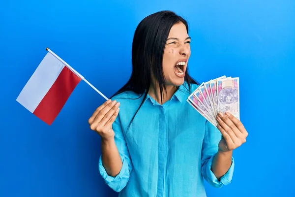年轻的拉丁女人拿着波兰国旗和兹罗提钞票 怒气冲冲地尖叫着 怒气冲冲地大叫着 愤怒和好斗的概念 — 图库照片