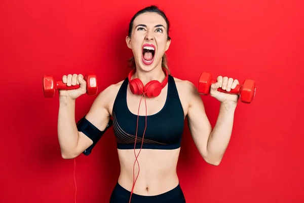 Young Hispanic Girl Wearing Sportswear Using Dumbbells Headphones Angry Mad — Zdjęcie stockowe