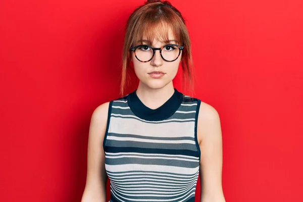 红头发的年轻女人穿着休闲装 戴着一副严肃的表情的眼镜 简单而自然地看着相机 — 图库照片