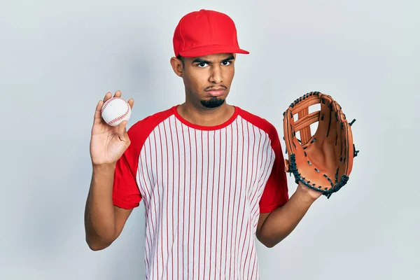 Joven Hombre Afroamericano Vistiendo Uniforme Béisbol Sosteniendo Guante Bola Escéptico —  Fotos de Stock