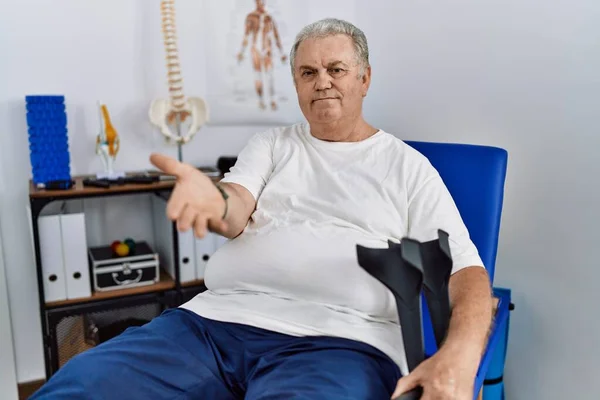 Homem Caucasiano Sênior Clínica Fisioterapia Segurando Muletas Sorrindo Alegre Oferecendo — Fotografia de Stock