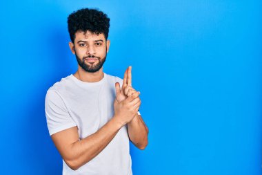 Sakallı, beyaz tişörtlü, el hareketleriyle sembolik silah tutan, cinayet silahlarıyla oynayan, sinirli yüzlü genç bir Arap. 