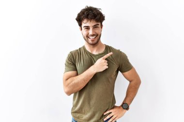 Hispanik adam izole edilmiş beyaz arka planda neşeli, yüzünde bir gülümseme, mutlu ve doğal bir ifadeyle elini ve parmağını kaldırmış duruyor. 