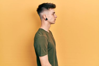Young caucasian boy with ears dilation wearing casual green t shirt looking to side, relax profile pose with natural face with confident smile. 