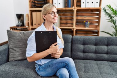 Genç sarışın psikolog elinde bir dosya, klinikteki koltukta oturuyor.