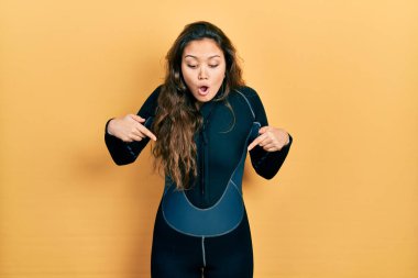Genç İspanyol kız dalgıç neoprene üniforması giyiyor. İlan veren parmaklarıyla işaret ediyor. Şaşırmış yüz ve ağzı açık. 