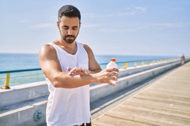 Spor yapan İspanyol sporcu güneşli bir günde koluna güneş kremi sürüyor.