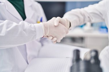 Laboratuvarda bilim adamı üniforması giyen kadın ve erkek el sıkışıyor.