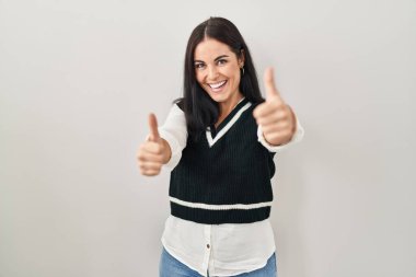 Tecrit edilmiş arka planda duran genç İspanyol kadın elleriyle olumlu bir jest yapmayı onaylıyor, gülümsüyor ve başarı için mutlu. kazanan jest. 