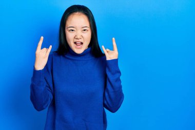 Genç Çinli kız gündelik giysiler içinde çılgın bir ifadeyle bağırıyor elleri havada rock sembolü yapıyor. Müzik yıldızı. ağır kavram. 