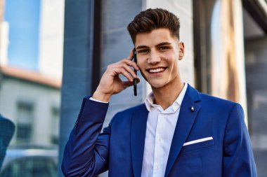 Akıllı telefondan konuşan genç adam sokakta takım elbise giyiyor.