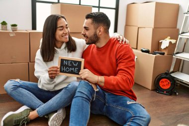 Genç Latin çift gülümsüyor. Yeni ev mesajıyla birlikte ellerinde tahtayla mutlu görünüyorlar..