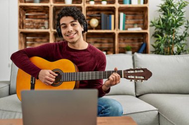 Genç İspanyol adam evdeki kanepede oturmuş online klasik gitar dersi alıyor..