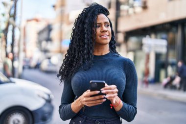 Afro-Amerikalı kadın sokakta akıllı telefon kullanarak kendine güveniyor.