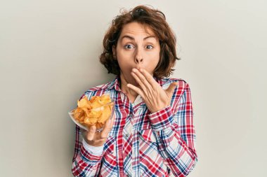 Elinde patates cipsi tutan genç esmer kadın ağızlarını eliyle kapatıyor, şokta ve hata yapmaktan korkuyor. şaşırmış ifade 