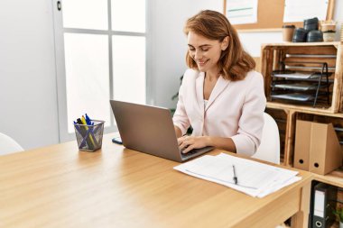 Ofiste çalışırken dizüstü bilgisayarla gülümseyen beyaz bir iş kadını..