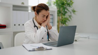 Klinikte çalışan, doktor üniforması giyen orta yaşlı İspanyol kadın.