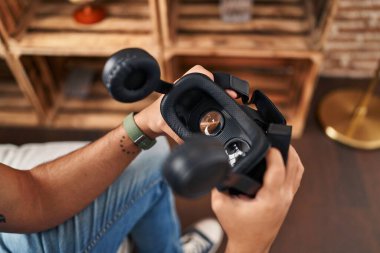Young hispanic man holding virtual reality goggles at home
