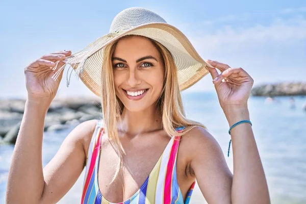 年轻的金发姑娘穿着泳衣 戴着夏帽 在海滩上开心地笑着 — 图库照片