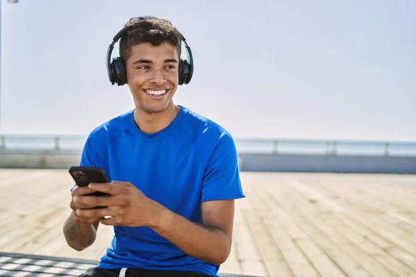 若いヒスパニック系の男の訓練は屋外でヘッドフォンを身に着けている音楽を聴く — ストック写真