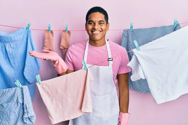 Joven Hombre Hispano Guapo Usando Delantal Más Limpio Sosteniendo Ropa —  Fotos de Stock