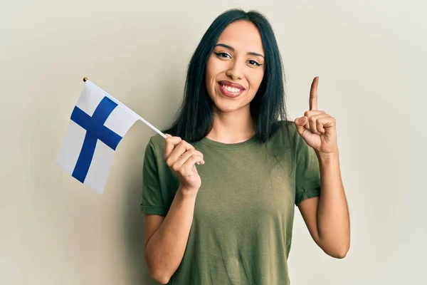 年轻的惊慌失措的女孩举着芬兰国旗微笑着 带着一个想法或问题指指点点着幸福的脸 排名第一 — 图库照片