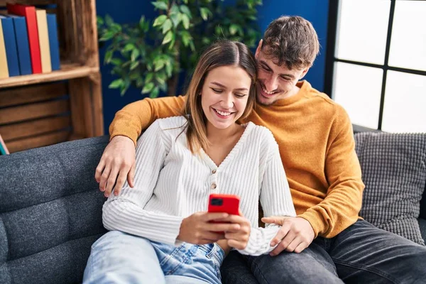 若い男と女のカップル使用スマートフォン座って上のソファに家 — ストック写真