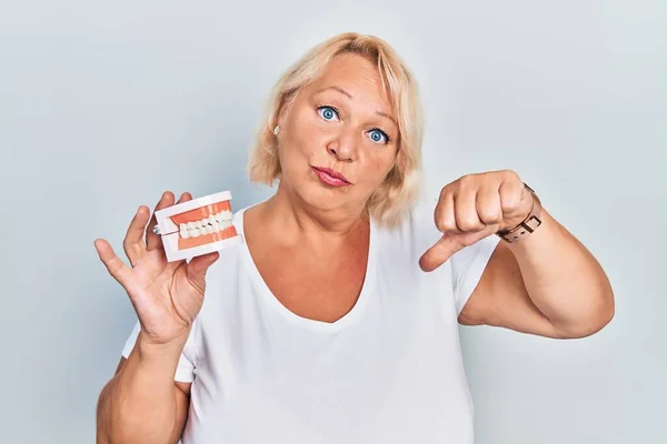 Mulher Loira Meia Idade Segurando Dentadura Com Rosto Irritado Sinal — Fotografia de Stock