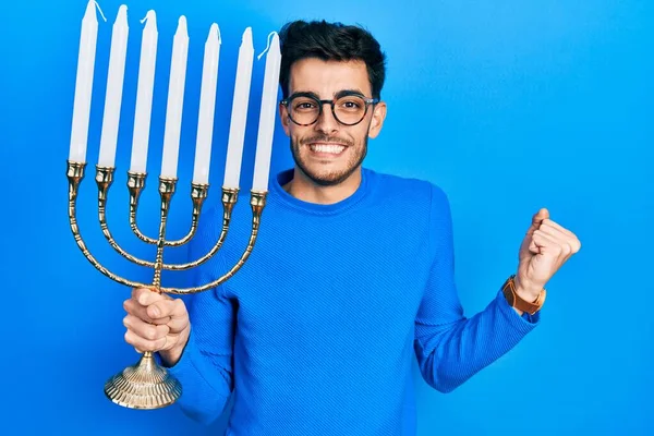 Young Hispanic Man Holding Menorah Hanukkah Jewish Candle Screaming Proud — Stock Photo, Image