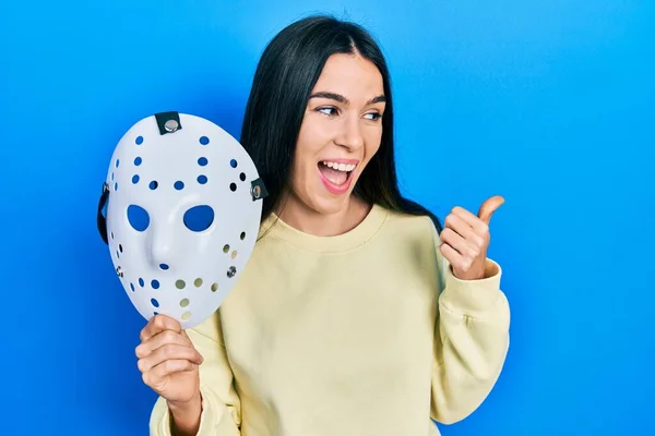 Young Brunette Woman Holding Hockey Mask Pointing Thumb Side Smiling — ストック写真