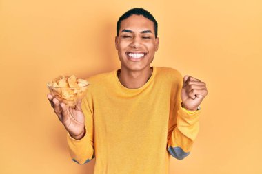 Genç Afrikalı Amerikalı patates cipsi tutan adam gururla bağırıyor, zaferi kutluyor ve kollarını kaldırdığı için çok heyecanlı. 