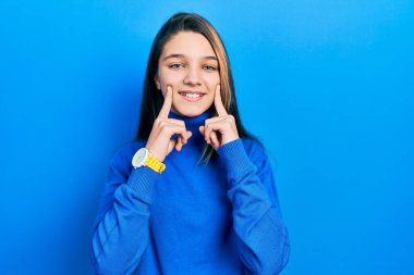 Balıkçı yaka kazak giyen genç esmer kız ağzı açık gülümseyen, parmakları işaret eden ve neşeli gülümsemeye zorlayan. 