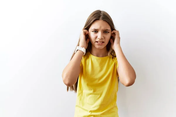 若いブルネットのティーンエイジャーは 大きな音楽のノイズのためにいらいらする表現で指で耳を覆う孤立した背景の上に一緒に立っています 聴覚障害の概念 — ストック写真