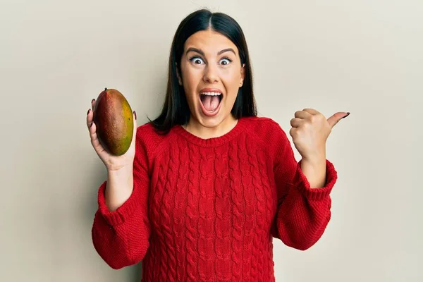Hermosa Morena Sosteniendo Mango Señalando Pulgar Hacia Lado Sonriendo Feliz —  Fotos de Stock