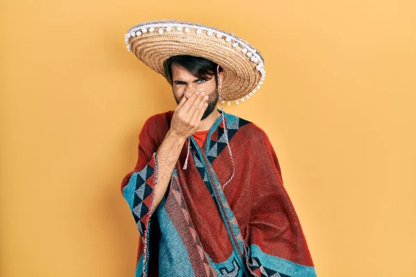 Jovem Hispânico Segurando Chapéu Mexicano Cheirando Algo Fedorento Nojento Cheiro — Fotografia de Stock