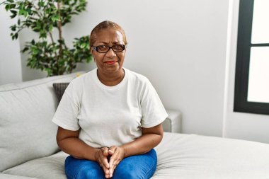 Evde kanepede oturan, kuşkucu ve gergin, sorunlardan dolayı suratını asan olgun İspanyol kadın. negatif kişi. 