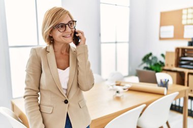 Orta yaşlı sarışın kadın, mimarlık stüdyosunda çalışan akıllı telefondan konuşuyor.