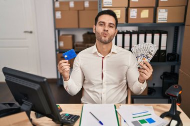 Küçük işletme şirketinde sakallı genç İspanyol bir adam elinde banknotlar ve kredi kartıyla kameraya bakıp öpüşürken sevimli ve seksi görünüyor. aşk ifadesi. 