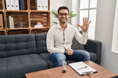 Danışma ofisinde çalışan sakallı genç İspanyol adam beş numarayı gösterip işaret ederken kendinden emin ve mutlu gülümsüyor.. 