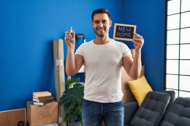 Sakallı, yeni evinin anahtarlarını tutan, yüzünde mutlu ve havalı bir gülümsemeyle gülümseyen genç İspanyol bir adam. diş gösterme. 